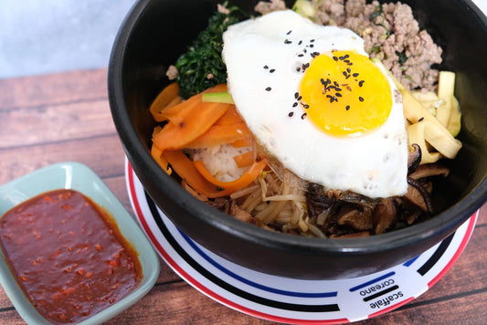 Piatto fumante di un delizioso Bibimbap tradizionale coreano con sfondo di legno e color blu e piatto di Scaffale Coreano