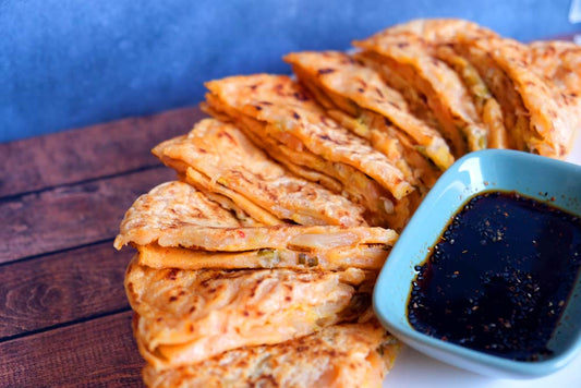 Piatto fumante di un delizioso Kimchi Jeon tradizionale coreano con sfondo di legno e color blu e piatto di Scaffale Coreano