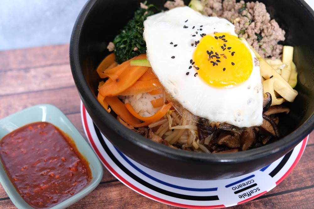 Piatto fumante di un delizioso Bibimbap tradizionale coreano con sfondo di legno e color blu e piatto di Scaffale Coreano 
