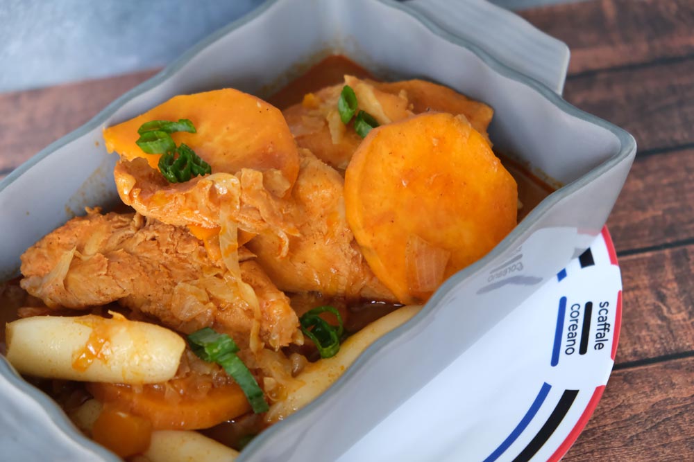 Piatto fumante di Dakgalbi, cioè pollo cucinato alla coreana, con sfondo di legno e color blu e piatto di Scaffale Coreano 