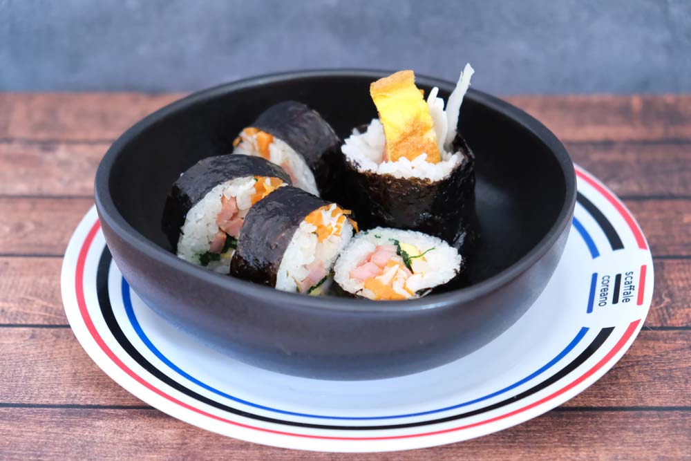 Rotolino tagliato di Gimbap (Kimbap) tradizionale coreano con sfondo di legno e color blu e piatto di Scaffale Coreano 