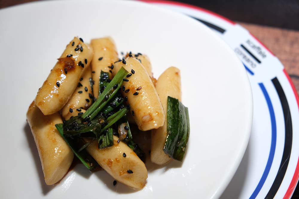 Piatto fumante di Tteokbokki non piccanti con sfondo di legno e color blu e piatto di Scaffale Coreano 