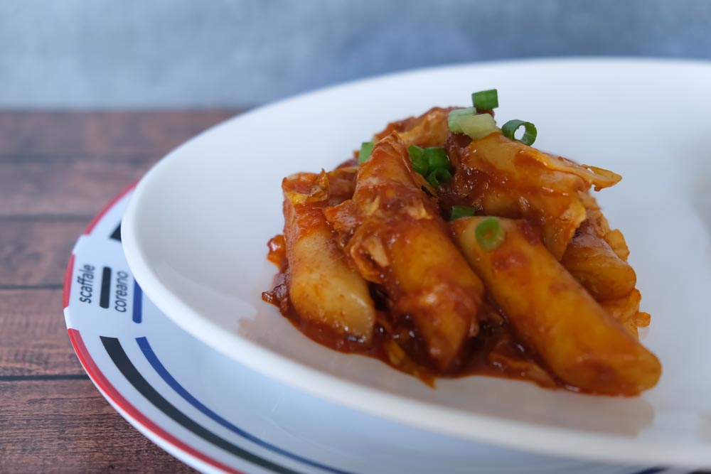Piatto fumante di Tteokbokki piccanti con sfondo di legno e color blu e piatto di Scaffale Coreano 