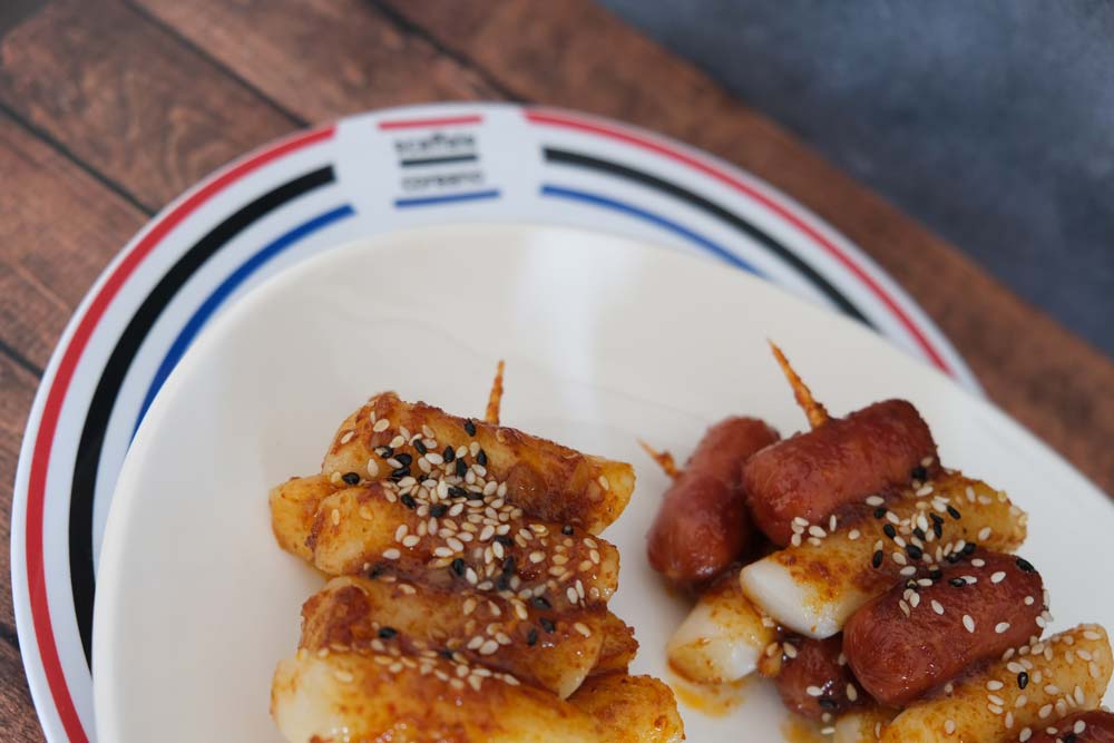 Spiedini di Tteokbokki (Tteokkochi) street food tradizionale coreano con sfondo di legno e color blu e piatto di Scaffale Coreano 