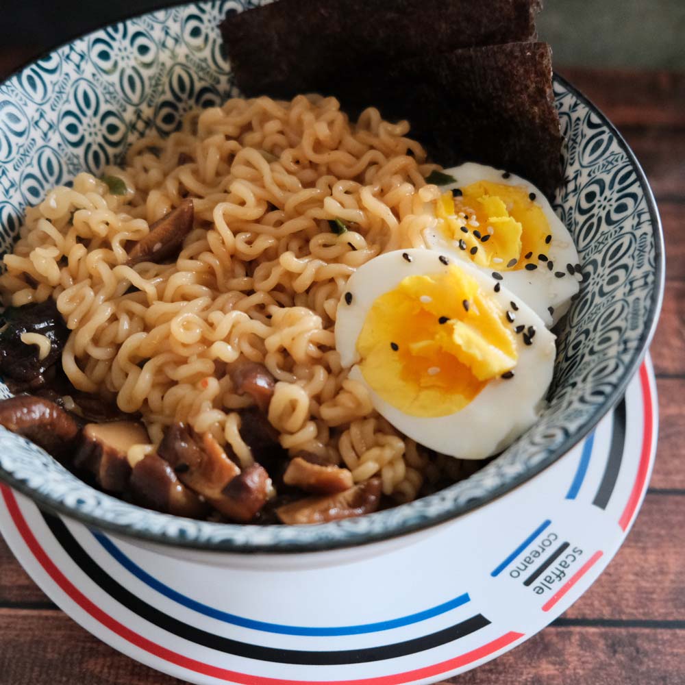 Piatto fumante di Ansung Tangmyun di Nongshim con sfondo blu e legno e piatto di Scaffale Coreano