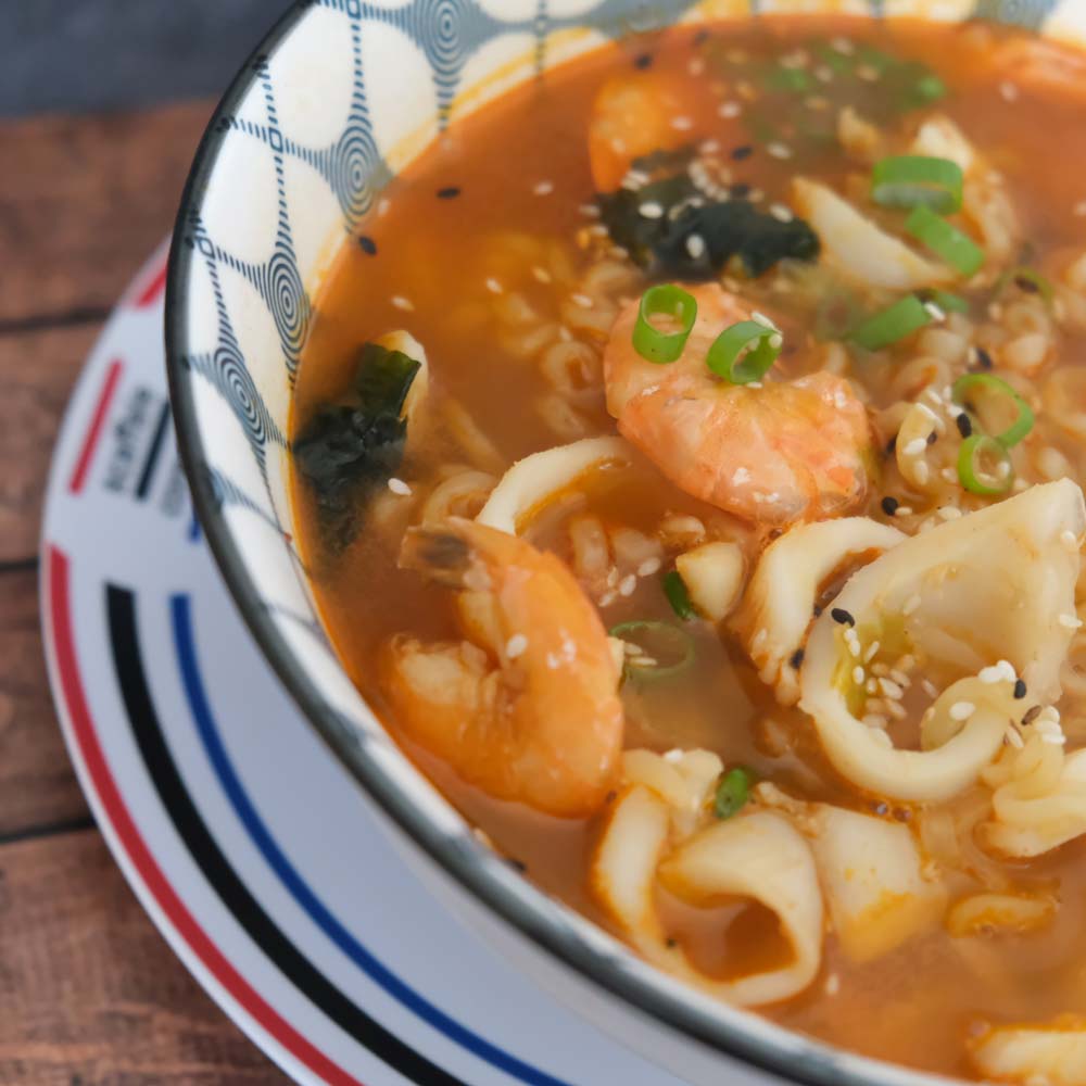 Piatto fumante di Champong Ramyeon di Nongshim con sfondo blu e legno e piatto di Scaffale Coreano