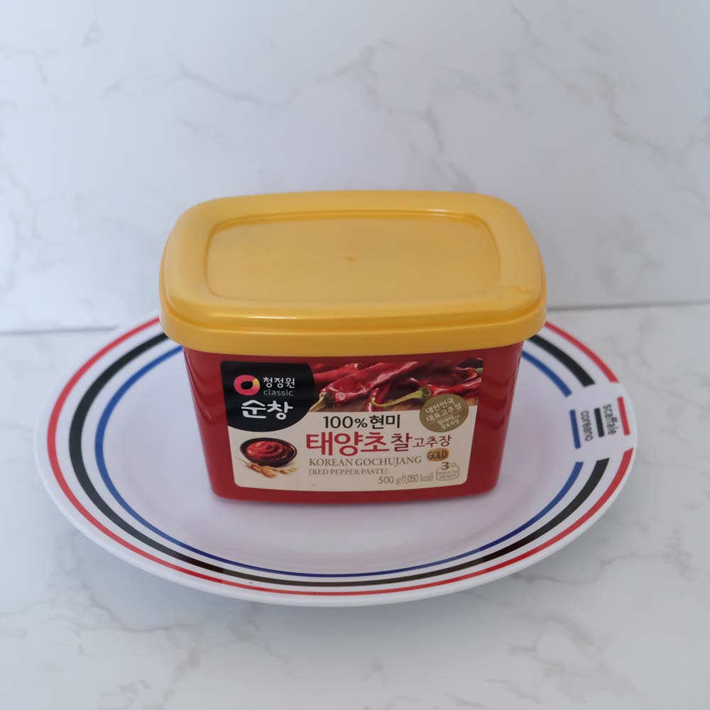 Gochujang pasta al peperoncino di Daesang Gochujang pasta al peperoncino di Sempio con sfondo marmo e piatto di Scaffale Coreano