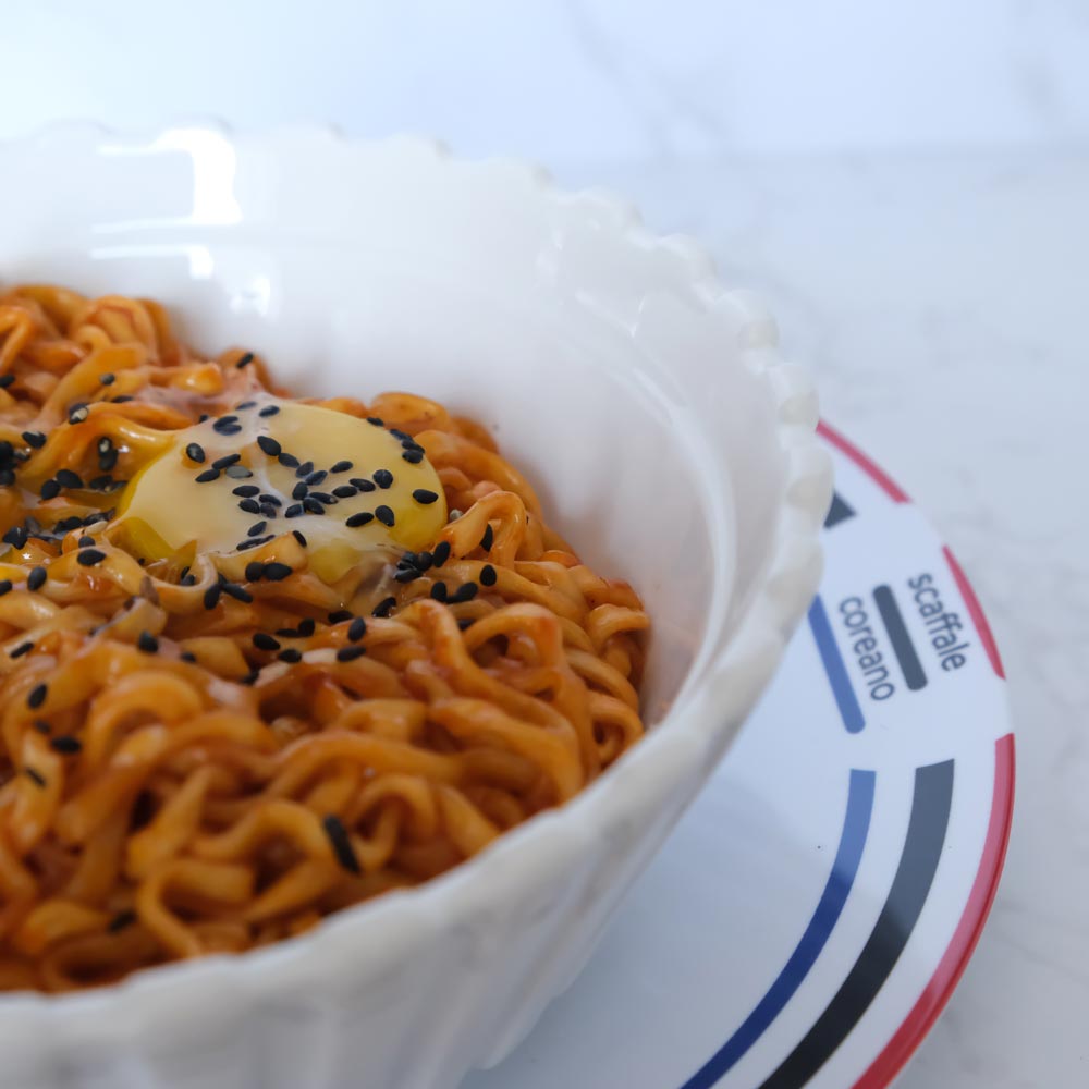 Piatto fumante di Hot Chicken Cheese Buldak Ramen di SamYang con sfondo marmo e piatto di Scaffale Coreano