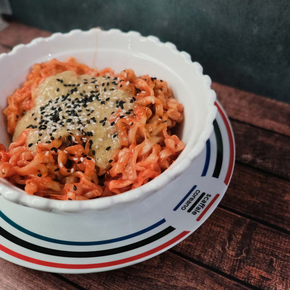 Piatto fumante di Hot Chicken Noodles Carbonara Buldak di SamYang con sfondo blu e legno e piatto di Scaffale Coreano