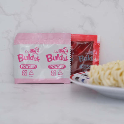 Contenuto della busta Hot Chicken Noodles Carbonara Buldak di SamYang con sfondo marmo e piatto di Scaffale Coreano