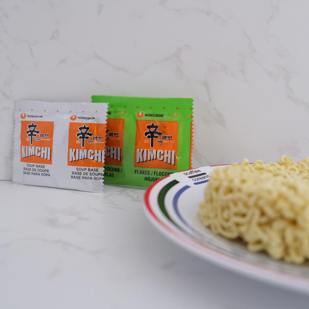 Cosa contiene la busta di Kimchi Shin Ramyun di Nongshim con sfondo marmo e piatto di Scaffale Coreano