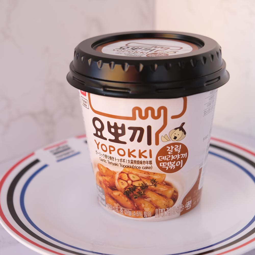 Yopokki Aglio Teriyaki Cup con sfondo marmo e piatto di Scaffale Coreano