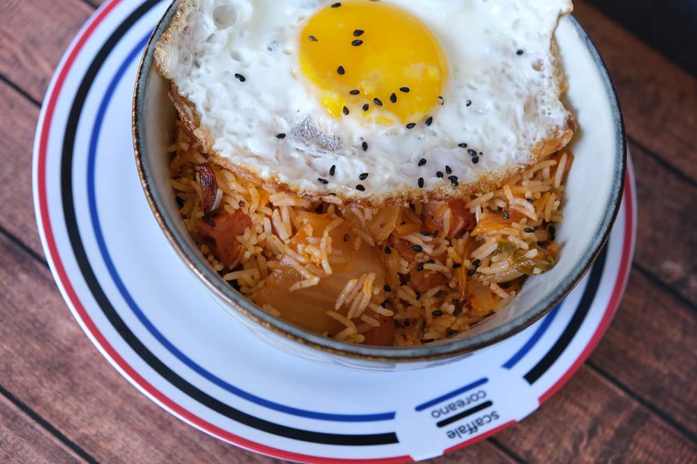 Piatto fumante di riso fritto al Kimchi con sfondo blu e piatto di Scaffale Coreano