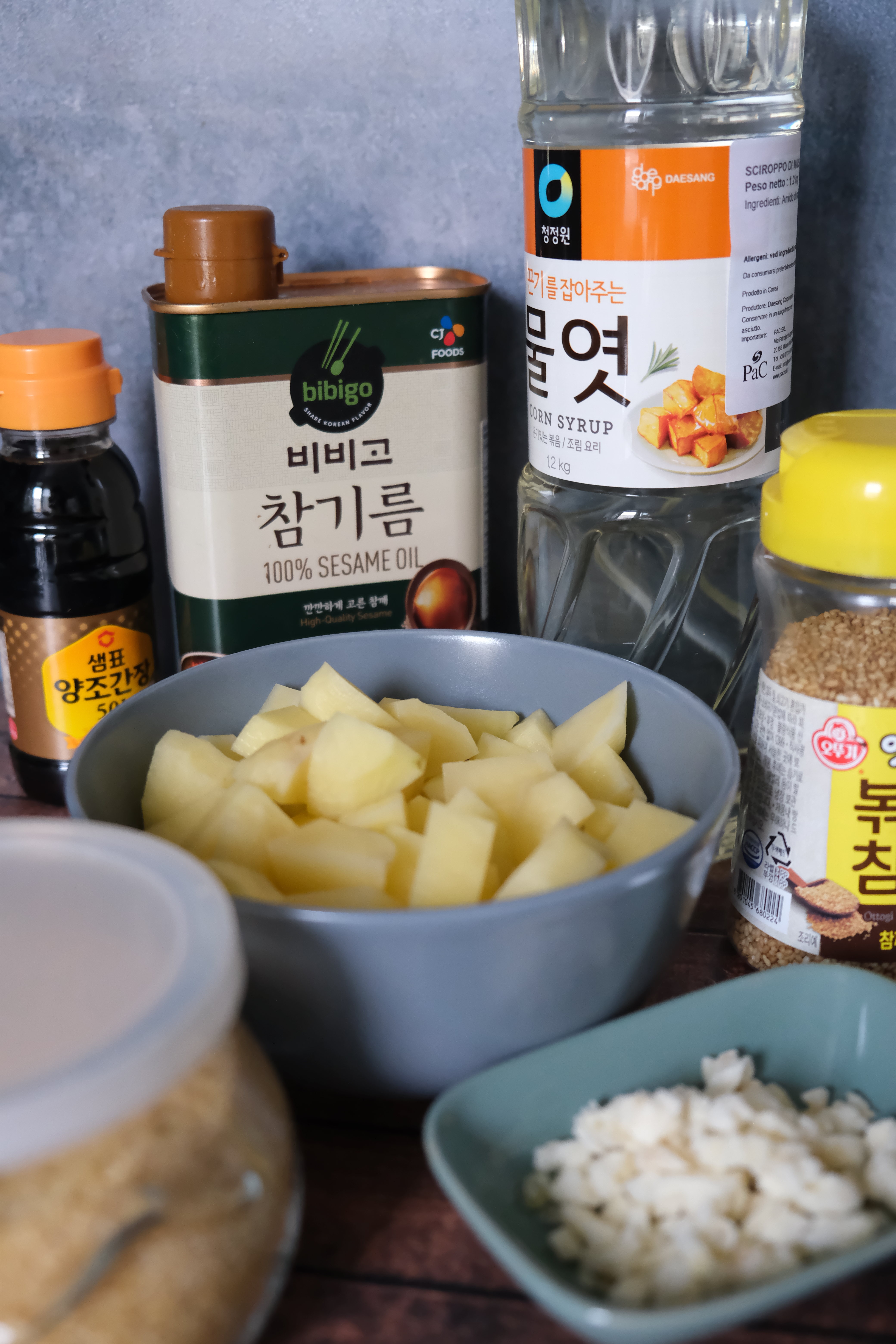 Una foto in cui sono presenti gli ingredienti usati in questa ricetta: salsa di soia, olio di sesamo, sciroppo di mais, semi di sesamo, aglio, zucchero e patate